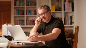 Picture of man sitting at a desk on a phone with a laptop