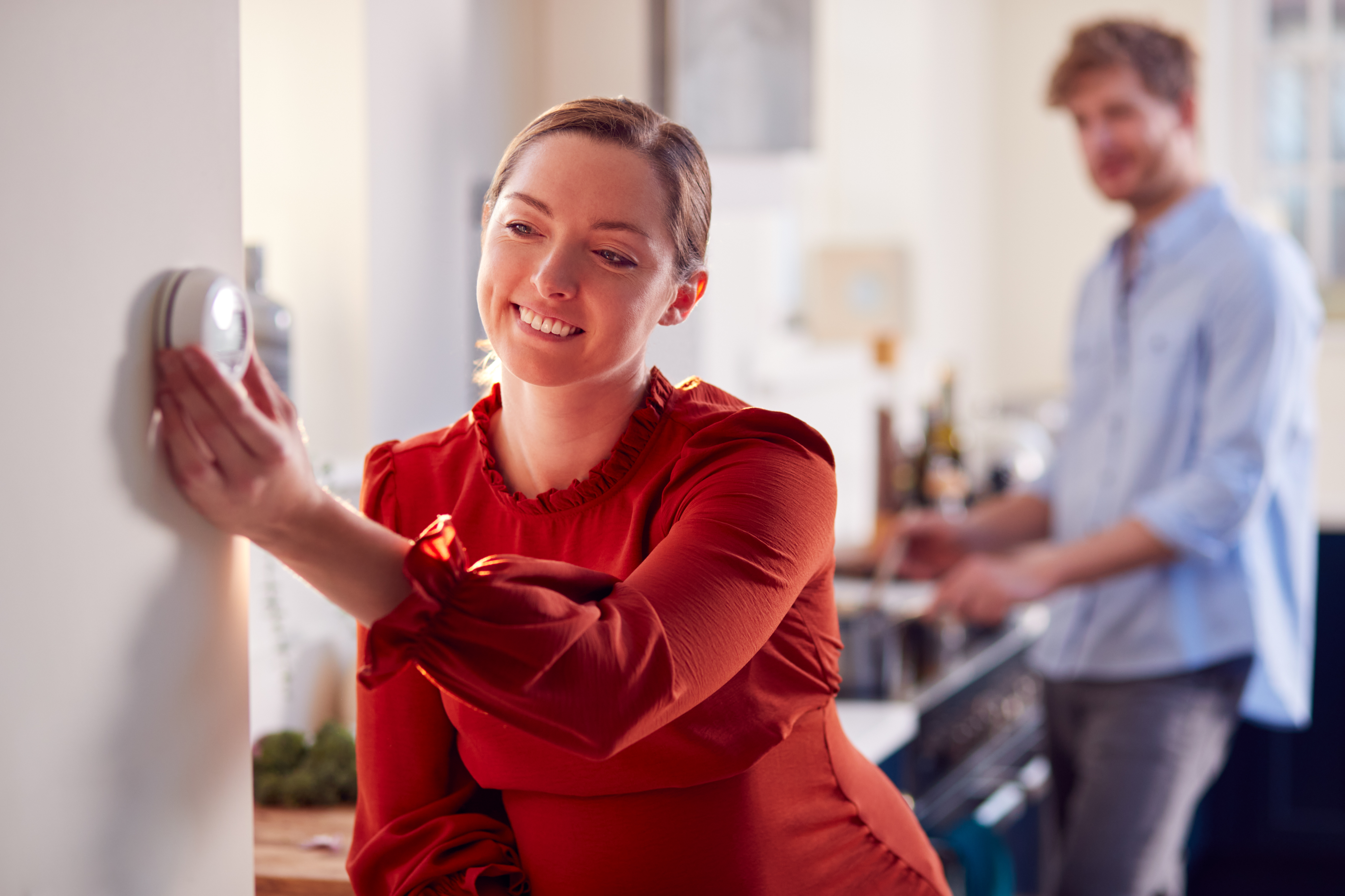 Picture of a smiling lady in red jumper turning down a thermostat