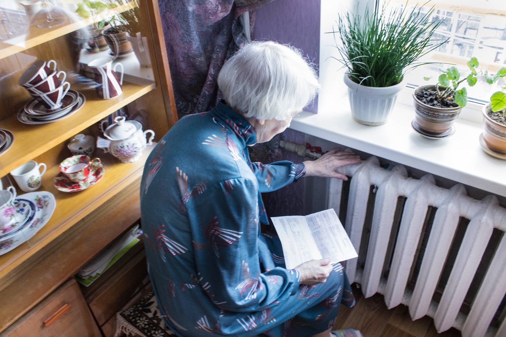 Elderly woman holds her hand against her heater