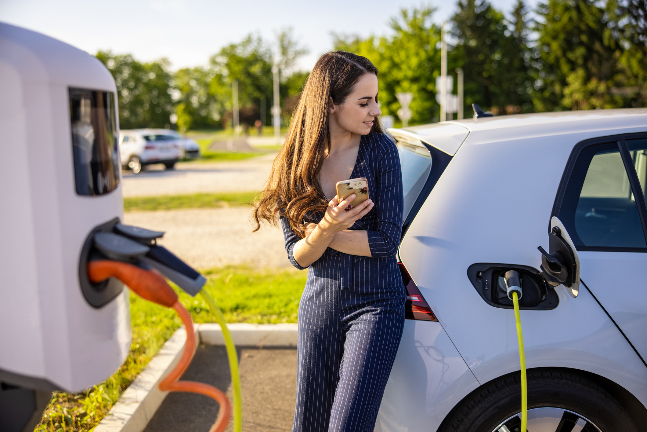 woman using a phone while an electric car charges
