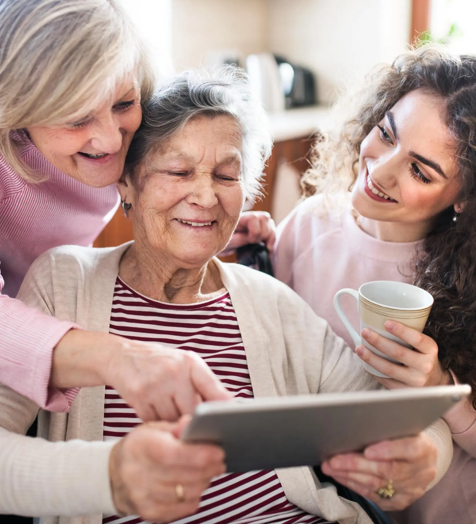 Elderly woman looking at an iPad with two other women sitting on either side of her and smiling 