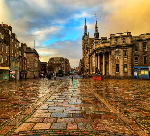 Castlegate in Aberdeen on a rainy day, the wet paving stones are reflecting the sunlight coming from the spaces in-between the clouds. 