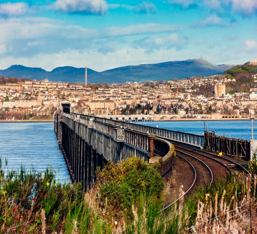 A picture of the Tay Rail Bridge on a sunny day, Dundee can be seen from across the water.