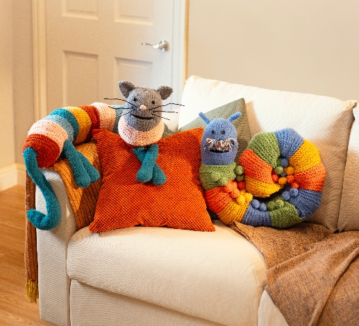 Kat the Cat and Doug the Caterpillars, colourful striped draught excluders, lie curled up on the sofa.