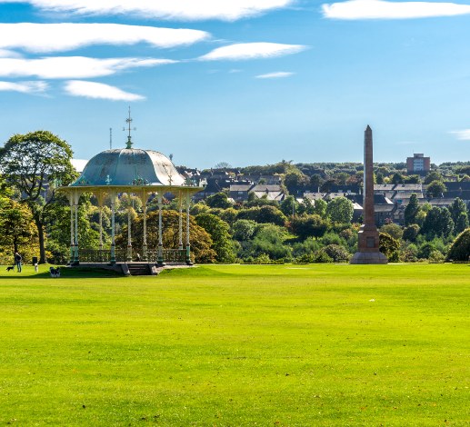 Duthie Park in Aberdeen featuring a bandstand, open green space and an obelisk under a blue sky.