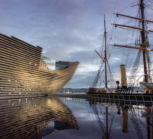 V&A Dundee and a historic sailing ship reflected in water along Dundee's waterfront.
