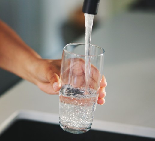 Water flowing from a kitchen tap into a clear drinking glass held beneath it.