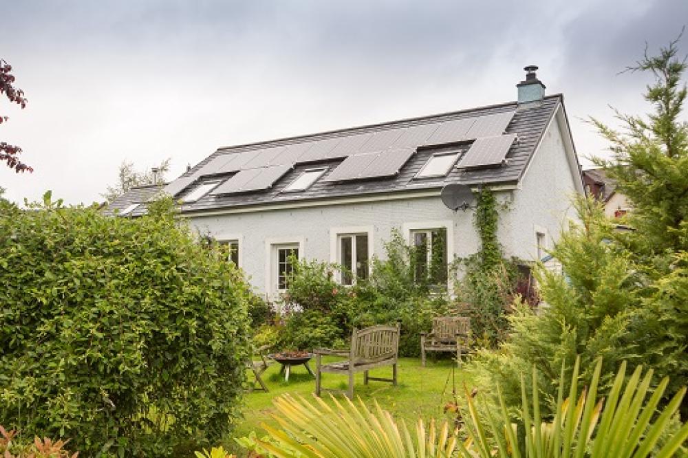 Picture of a large white house with solar panels on the roof in a country garden