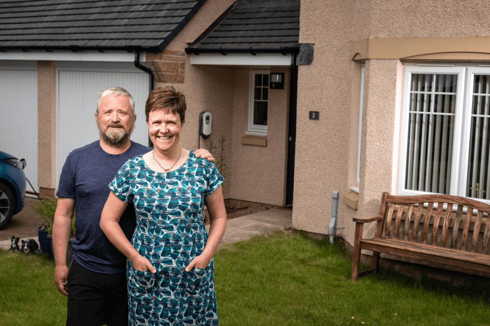David and Pauline standing in front of their house smiling