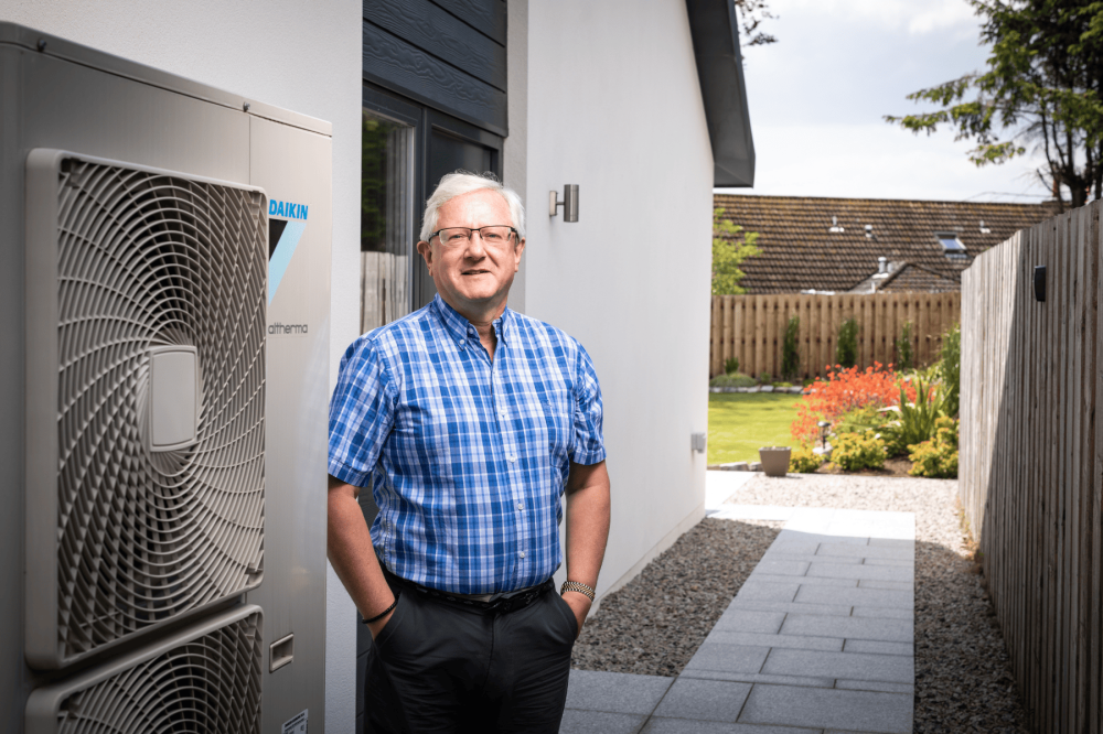 Gordon standing beside his heat pump at his home smiling