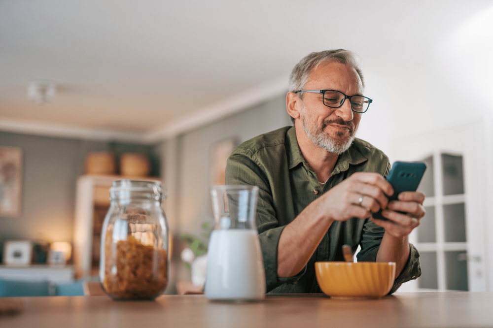A man sitting in the kitchen smiling at his phone