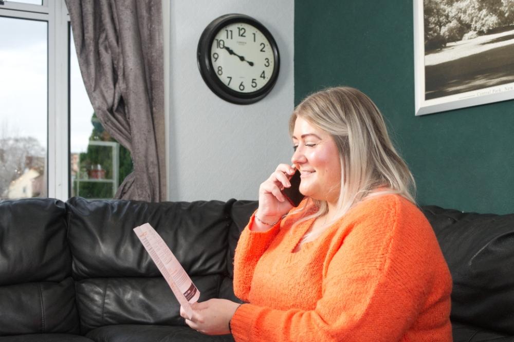 A person on the phone is smiling; they are reading a Home Energy Scotland leaflet.
