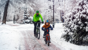 A man and child cycling in winter in a snowy forest